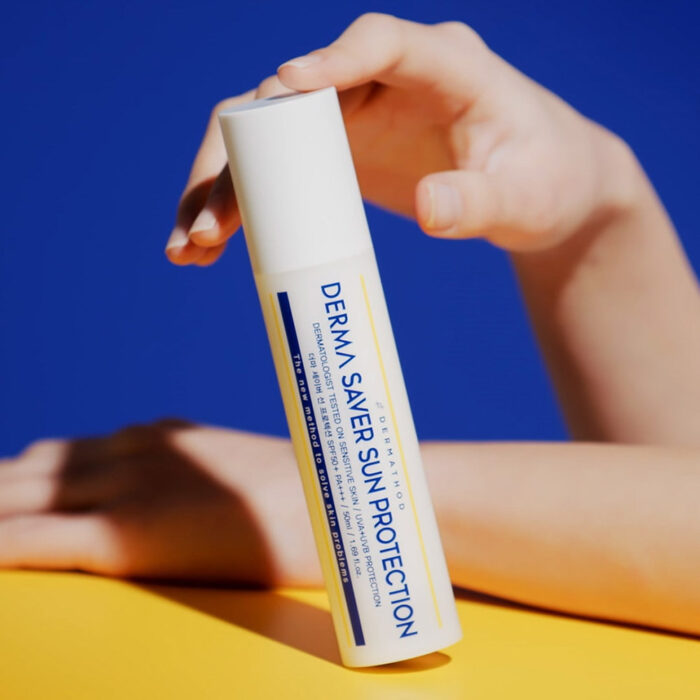 DERMATHOD Derma Saver Sun Protection – schlanke weiße Sonnenpflegeflasche mit blauen und gelben Akzenten, stehend auf hellem Hintergrund.