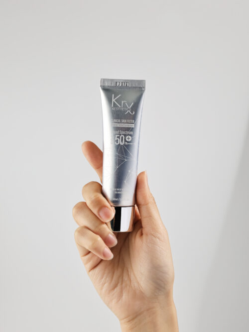 Hand hält KrX Aesthetics Tinted Sun Protection Tube – hochwertiger Sonnenschutz SPF 50+ PA++++, 30 ml, ideal für tägliche Anwendung mit getönter Textur.